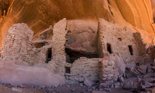 Ancient stone ruins nestled under a rocky overhang, showcasing weathered walls and remnants of a bygone civilization.
