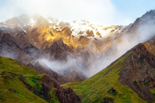 Majestic mountains with snow-capped peaks, shrouded in mist and surrounded by lush green slopes.