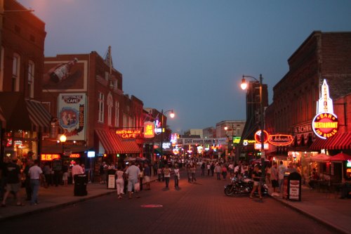 A lively street scene at dusk, filled with neon signs, cafes, and people enjoying the vibrant atmosphere.