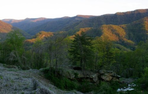 A scenic view of rolling mountains and lush greenery under a soft sunset glow.