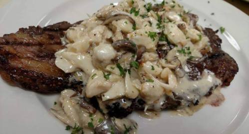 A plate of steak topped with creamy mushroom and seafood sauce, garnished with fresh parsley.