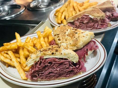 Two plates of sandwiches filled with stacked slices of roast beef, served with crispy French fries.