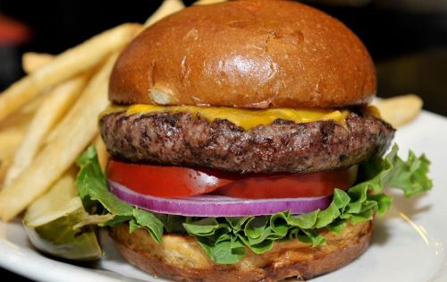 A juicy cheeseburger with lettuce, tomato, onion, and a side of golden fries on a white plate.