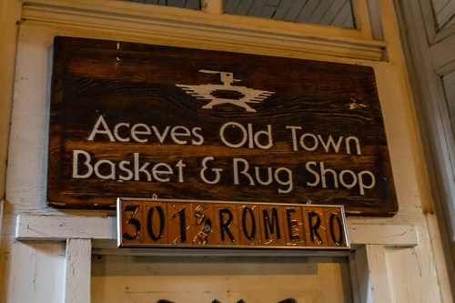 Wooden sign for Aceves Old Town Basket & Rug Shop, with the address 301 Romero displayed below.