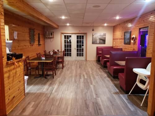 Cozy restaurant interior with wooden walls, booths, tables, and a view of double doors leading outside.