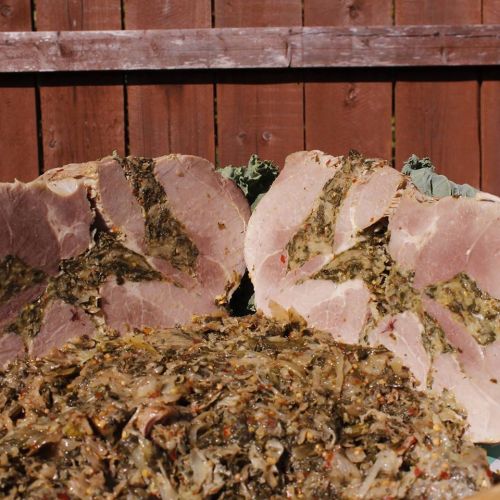 Sliced ham with a green herb filling, served alongside a mound of seasoned greens on a wooden background.
