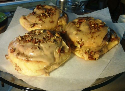 Three large cinnamon rolls topped with caramel icing and chopped pecans, placed on a round tray with parchment paper.