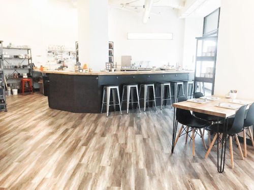 Modern restaurant interior featuring a curved bar, high stools, and wooden tables with black chairs on a wooden floor.