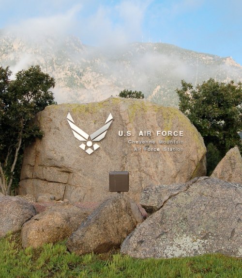 Sign for U.S. Air Force Cheyenne Mountain Air Force Station on a large rock, surrounded by trees and mountains.