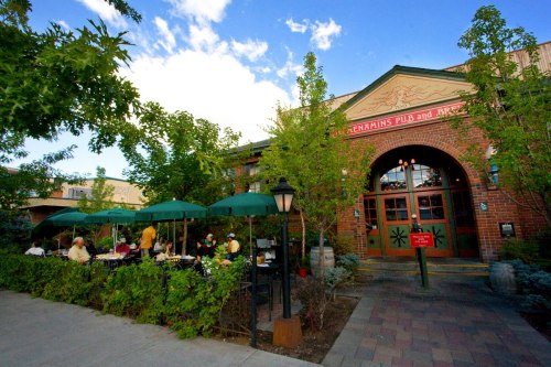 A brick building with green umbrellas over outdoor seating, surrounded by trees and a clear blue sky.