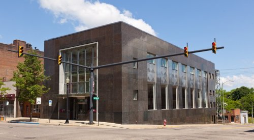 Modern black stone building at a street intersection with traffic lights and clear blue sky.