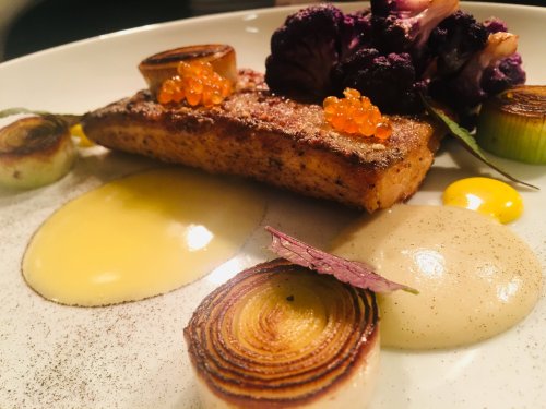 A beautifully plated dish featuring seared fish, vibrant vegetables, and garnishes, showcasing a mix of textures and colors.