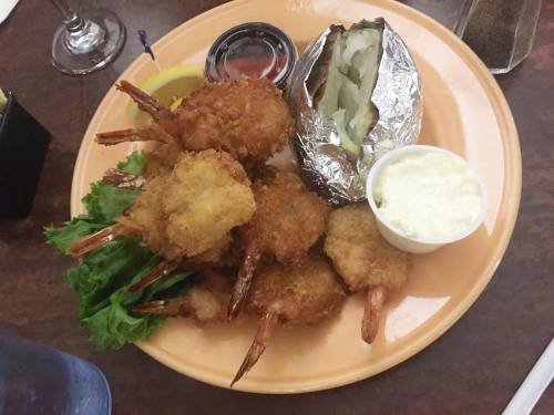 A plate of crispy fried shrimp with a baked potato, lemon wedge, and dipping sauce, garnished with lettuce.