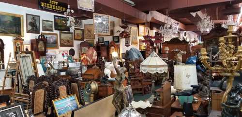 A cluttered antique shop filled with various vintage items, including furniture, paintings, and decorative pieces.