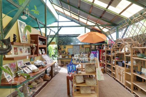 Bright, airy shop interior with wooden shelves, art displays, and a large orange umbrella, surrounded by greenery.