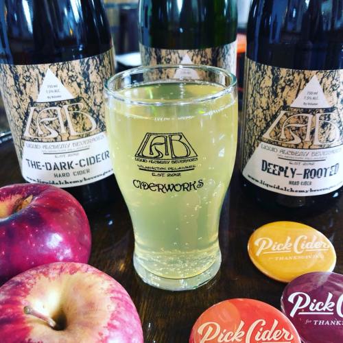 A glass of hard cider in front of two bottles and apples, with cider-themed coasters nearby.