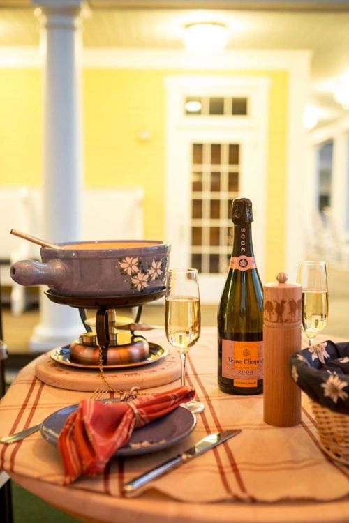 A cozy table setting with a fondue pot, champagne bottle, two glasses, and a plate, all against a warm, inviting background.