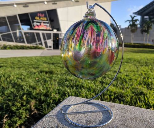 A colorful glass orb on a metal stand, set against a grassy area and a building in the background.