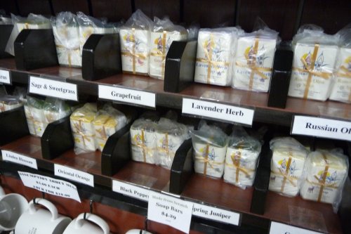 Shelves displaying various packaged soaps labeled with scents like Sage & Sweetgrass, Grapefruit, and Lavender Herb.