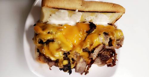 A hearty sandwich filled with pulled meat, melted cheddar cheese, and creamy sauce on a soft bun.