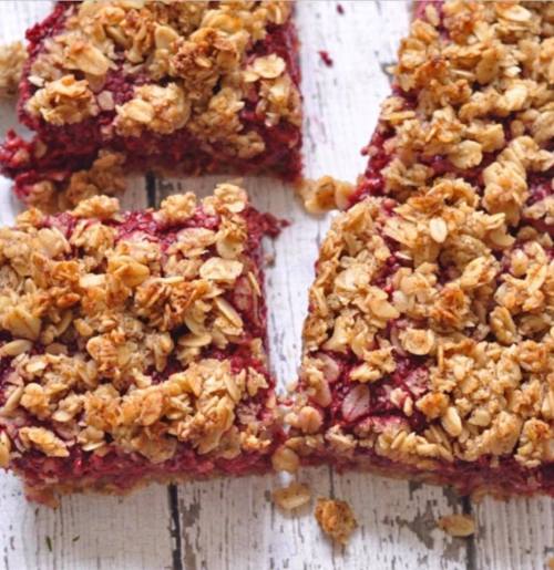 Close-up of berry crumble bars topped with golden oat granola, cut into squares on a rustic wooden surface.