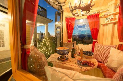 Cozy interior of a small cabin with a table, chairs, and warm lighting, overlooking a scenic view at dusk.