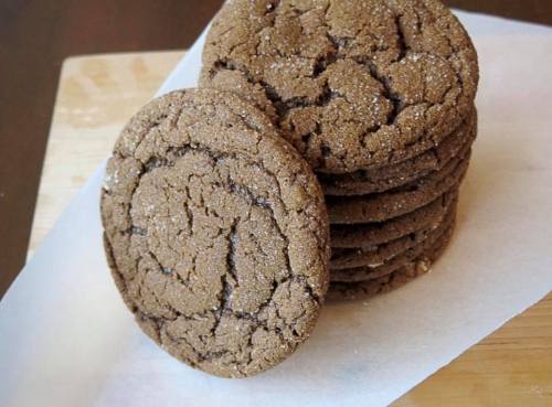 A stack of brown, crinkly cookies dusted with sugar on a parchment-lined surface.
