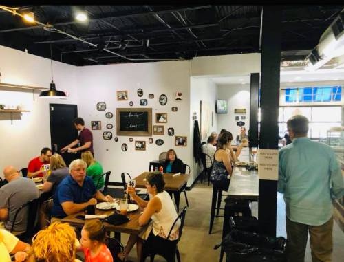A busy restaurant interior with diners at tables, wall decor, and staff serving food in a casual atmosphere.