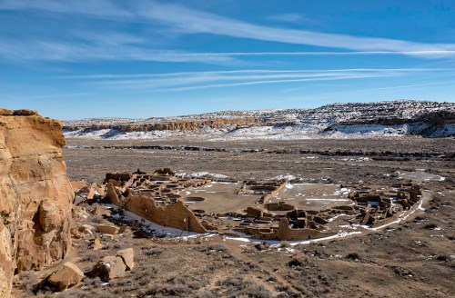 Ancient ruins in a desert landscape, surrounded by snow-capped hills and a clear blue sky.