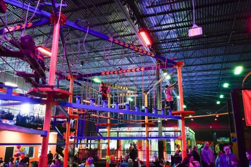 A vibrant indoor adventure park with colorful climbing structures and people navigating the ropes course.