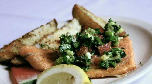 A plate featuring grilled salmon topped with fresh salsa, served with potato wedges and a lemon slice.