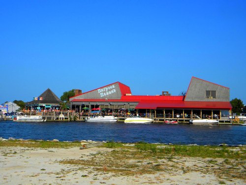 A waterfront restaurant with a red roof, surrounded by boats and clear blue skies.