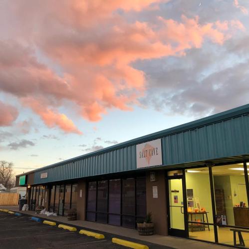 A building with a teal roof and sign reading "Salt Cave," under a colorful sunset sky with pink clouds.