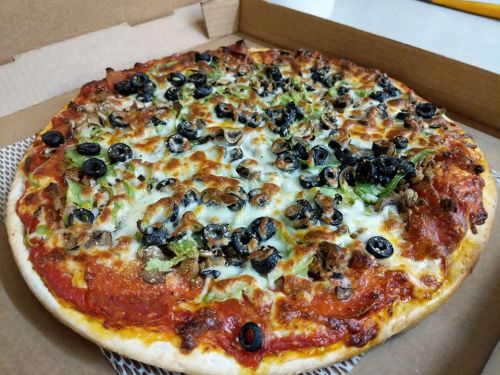 A freshly baked pizza topped with olives, mushrooms, and green peppers, in a cardboard pizza box.