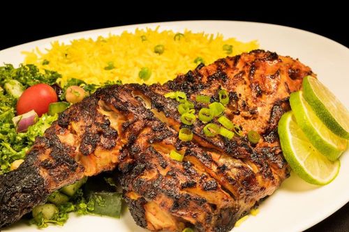 Grilled chicken with green onions, served with yellow rice, salad, and lime wedges on a white plate.