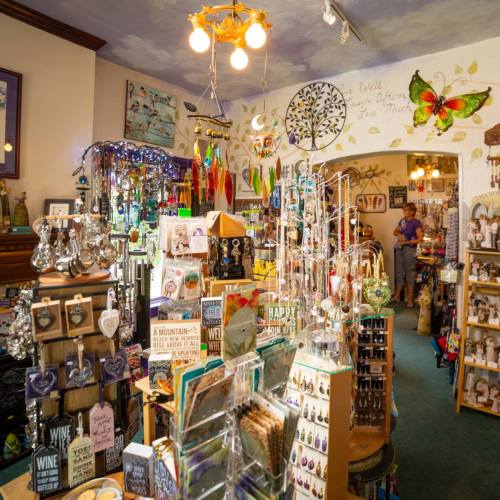 A colorful gift shop filled with various decorations, jewelry, and trinkets, with a customer browsing in the background.