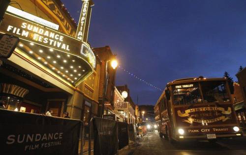 A vintage trolley bus near the Sundance Film Festival marquee, with festive lights illuminating the street at dusk.