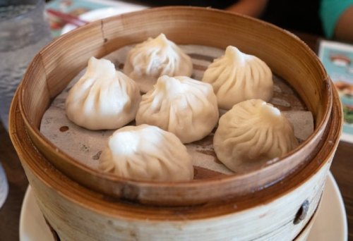 A bamboo steamer filled with eight steamed dumplings, resting on a parchment liner.