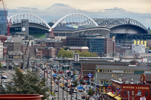 A view of Seattle's stadiums with Mount Rainier in the background, bustling streets filled with cars and buildings below.