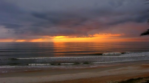 A serene beach at sunset, with waves gently lapping the shore under a colorful, cloudy sky.