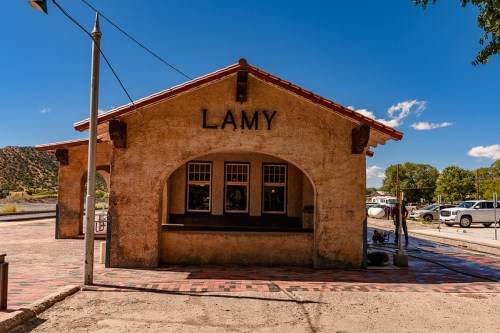 Historic Lamy train station with a stucco exterior and red tile roof, set against a clear blue sky.
