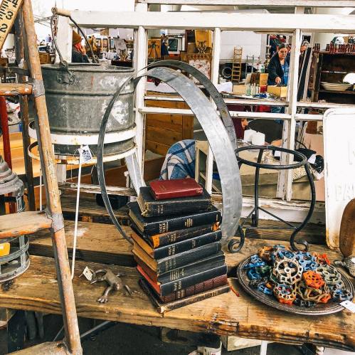 A stack of vintage books topped with a metal ring, surrounded by various antique items on a wooden table.