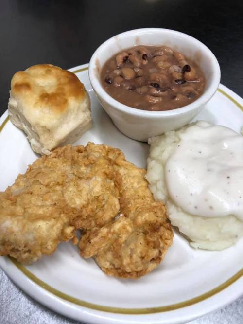 A plate of fried chicken, mashed potatoes with gravy, black-eyed peas, and a biscuit.