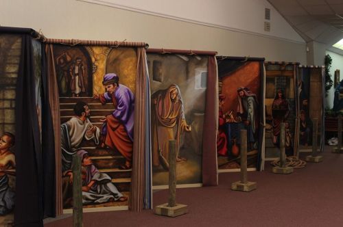 A series of large, colorful murals depicting biblical scenes, displayed on stands in a spacious indoor setting.