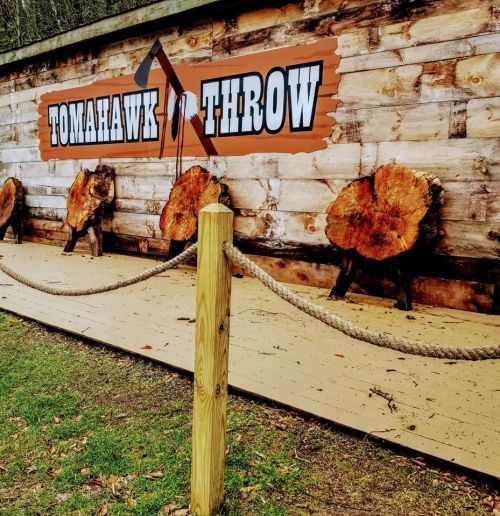 A wooden wall with the words "TOMAHAWK THROW" and three log targets for throwing tomahawks.