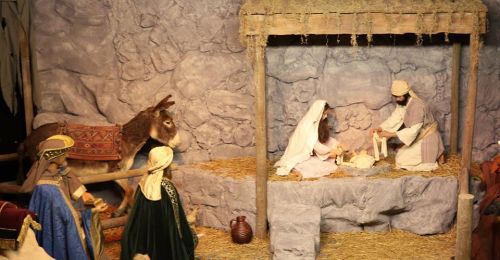 Nativity scene with Mary, Joseph, and baby Jesus in a stable, surrounded by a donkey and visitors.