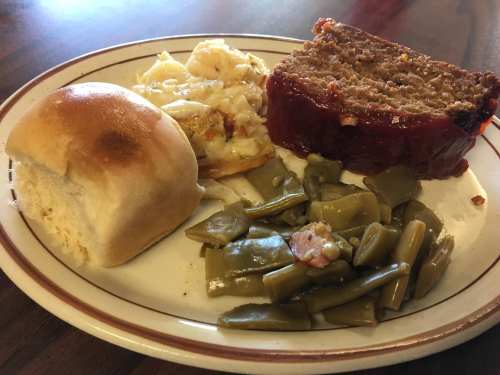 A plate with meatloaf, macaroni and cheese, green beans, and a roll.