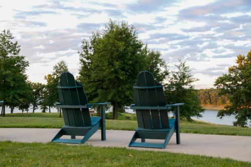 Two green Adirondack chairs facing a serene lake, surrounded by trees and a cloudy sky.