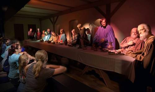 A group of people observes a lifelike diorama of the Last Supper, featuring figures seated at a long table.
