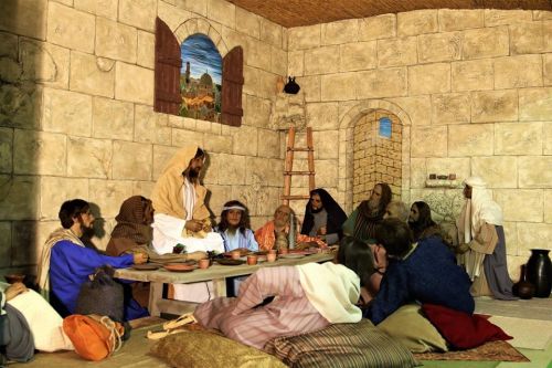 A group of people in historical attire gathered around a table in a stone-walled room, engaged in conversation.